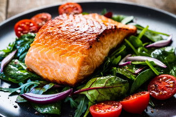 Fried salmon steak with vegetables on wooden table