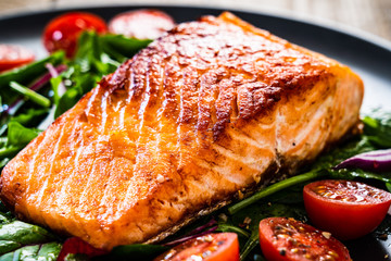 Fried salmon steak with vegetables on wooden table