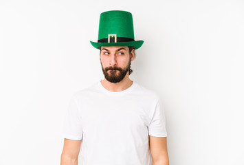 Young caucasian man wearing a saint patricks hat isolated confused, feels doubtful and unsure.
