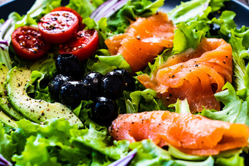 Salmon salad - smoked salmon and vegetables on black stone background
