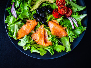 Salmon salad - smoked salmon and vegetables on black stone background