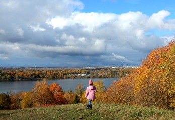 A girl in a pink jacket on a mountain in an autumn Park, at the bottom of the lake.