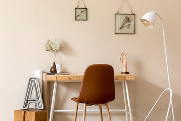 Minimalistic scandinavian interior of home office space with mock up photo frames, wooden desk, brown chair, design lamp, office and personal accessories. Stylish neutral home decor. Template.