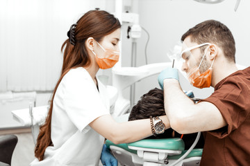 Fototapeta na wymiar A young male dentist doctor treats a patient. Medical manipulations in dentistry, surgery. Professional uniform and equipment of a dentist. Healthcare Equipping a doctor’s workplace. Dentistry