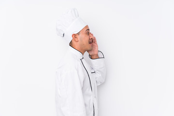 Young latin chef man isolated shouting and holding palm near opened mouth.