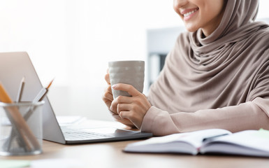 Unrecognizable islamic woman office employee drinking coffee at workplace