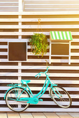 Fototapeta na wymiar Vintage old blue bicycle near a store or bakery wall with wooden white boards in a rustic style with chalkboard, signboards with sunshades, sunny morning vertical background.