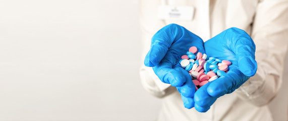 The doctors hands in blue medical gloves are stretched forward and hold multi-colored pills. Close-up medicine, vitamins and antibiotics for the treatment of health on light background, copy space.