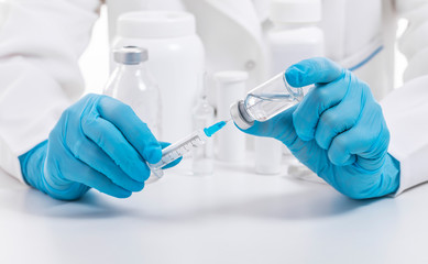 Unrecognizable doctor wearing medical protective mask and blue nitrile gloves fills syringe, cropped