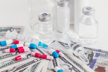 Stock of multicolored gelatin capsules, syringe, ampules, and medical vials on dollars banknotes