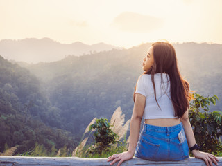 Relaxing in nature concept from backside of hipster girl sitting with enjoying the sunset on peak mountains in tropical rain forest.
