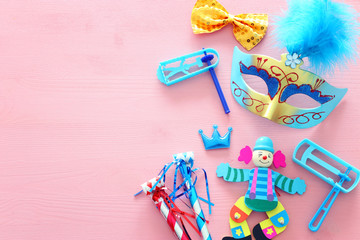 Party colorful noisemaker, mask and cute clown doll over pink wooden background. Top view, flat lay