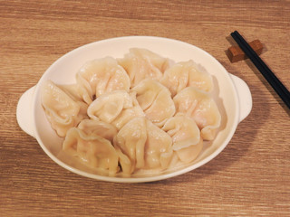 Top view of delicious hot boiled dumplings on white plate and bamboo chopsticks on wooden background .Boiled dumplings are traditional Asian homemade food. Taiwan food.