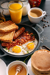 English breakfast on a dark table. fried eggs with bacon canned beans and sausage. near coffee,...