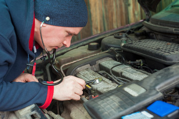 man with stethoscope checking car engine, auto service concept