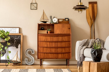 Stylish and vintage interior design of open space with wooden retro cabinet, design chair, sofa, map, paddle, ship, cacti, plants and elegant personal accessories. Template. Modern vintage home decor. © FollowTheFlow