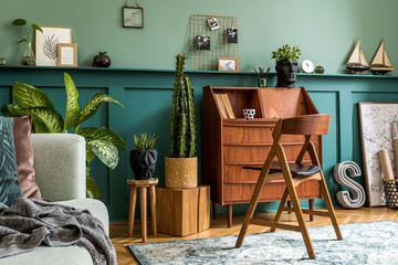 Modern and retro composition of home office interior with wooden cabinet, chair, plants, decoration and elegant personal accessories. Stylish vintage concept of home decor. Wood panelling. Template.