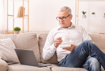 Elderly Man Looking At Laptop And Having Tea