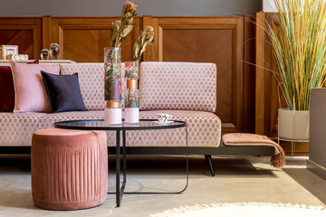 Stylish interior of living room with design pink sofa, elegant pouf, coffee table, flowers, pillows, decoration and elegant personal accessories. Modern home decor. Home staging. Template.  