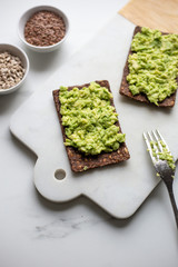 Healthy Snack from Wholegrain Rye Crispbread Crackers with Avocado on white marble background with copy space