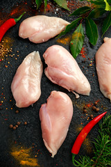 Raw free range chicken breast fillets with seasoning, fresh bay leaves, rosemary and chilies on black background
