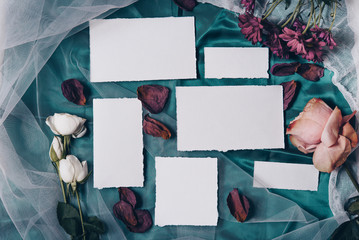 Wedding invitation mockup with roses, papers on white textile background. Top view, flat lay. Wedding stationary. Perfect for presentation of your invitation, menu, greeting cards