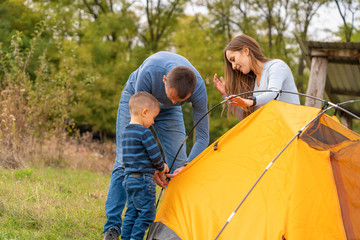 Happy family with little son set up camping tent. Happy childhood, camping trip with parents. A child helps to set up a tent