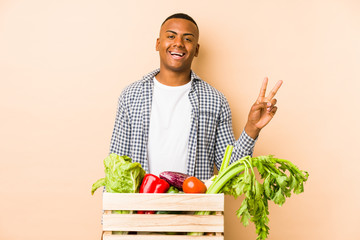 Young farmer man isolated on a beige background joyful and carefree showing a peace symbol with fingers.