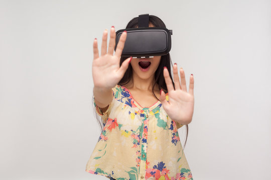 Surprised delighted woman in VR glasses standing with raised palms, playing video game saying wow, experiencing excited emotions while using virtual reality 3d headset. indoor studio shot, isolated