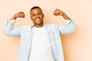 Young latin man isolated on beige background showing strength gesture with arms, symbol of feminine power