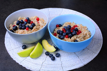 Oatmeal porridge with fresh blueberries in blue and grey bowls.  Next apple slice. Healthy breakfast, healthy eating, vegan food concept. Colorful breakfast for kids, selective focus, close up