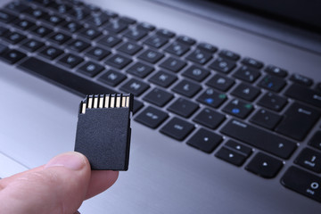 Hand holds flash drive,Micro SD memory card adapter on laptop background. close up