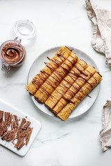 french crepe filled with caramel fudge and decorated with chocolate fudge, berries castor sugar and mint leaves on marble background with copy space