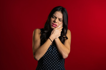 Young pretty latin woman with tooth pain on red studio background. Toothache, dental problems, stomatology and medicine concept.