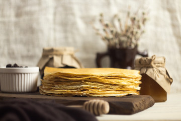A stack of fresh Russian pancakes for Shrovetide with jam, honey and willow branches. Pancake week. On a wooden Board in the Russian style