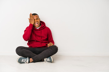 Young latin man sitting on the floor isolated having fun covering half of face with palm.