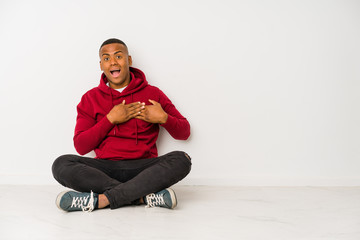 Young latin man sitting on the floor isolated laughing keeping hands on heart, concept of happiness.
