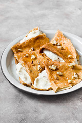 Crepes or thin pancakes with cottage cheese cream, honey and walnut. Traditional Maslenitsa (Shrovetide) meal and tasty breakfast on gray background. Copy space.