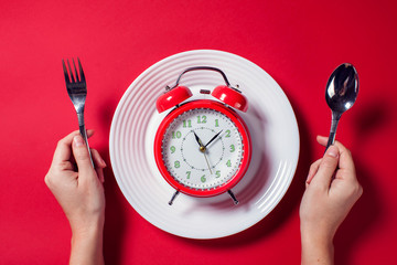 Alarm clock on the white plate with spoon and fork on the color background. Food and diet concept
