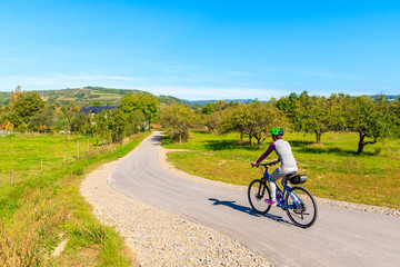 Young woman cycling on Velo Dunajec road among green hills with orchards near Nowy Sacz town,...