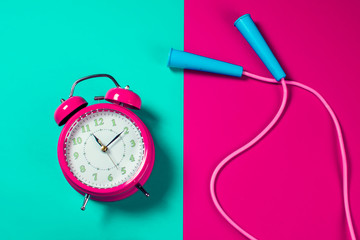 Alarm clock and jump rope on the color background. Fitness and healthcare concept