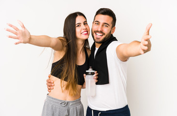 Young caucasian fitness couple isolated feels confident giving a hug to the camera.