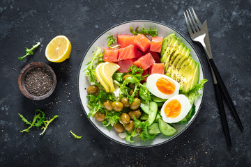 Ketogenic, paleo diet lunch bowl with salted salmon fish, lemon, avocado, olives, boiled egg, cucumber, green lettuce salad and chia seeds, healthy food trend, top view