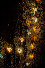 Blurred heart-shaped gold lights behind wet glass