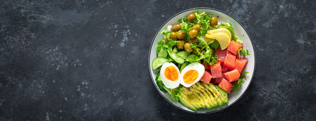 Ketogenic, paleo diet lunch bowl with salted salmon fish, lemon, avocado, olives, boiled egg, cucumber, green lettuce salad and chia seeds, healthy food trend, top view