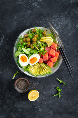 Fototapeta na wymiar Ketogenic, paleo diet lunch bowl with salted salmon fish, lemon, avocado, olives, boiled egg, cucumber, green lettuce salad and chia seeds, healthy food trend, top view