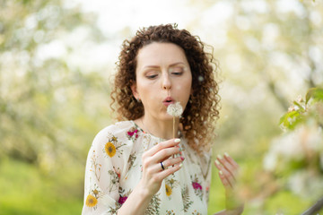 Pretty girl blowing dandelion in summer park. Green grass beautiful nature. Pure emotion.