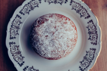 Fresh homemade jelly filled doughnut on a plate, covered in powdered sugar, above view