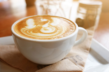 Hot latte art in white cup and dry flowers decoration in glass in natural sunlight at cafe