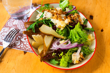 Salad with pear, cheese, onion, lettuce and rucola on plate, towel and glass of water .